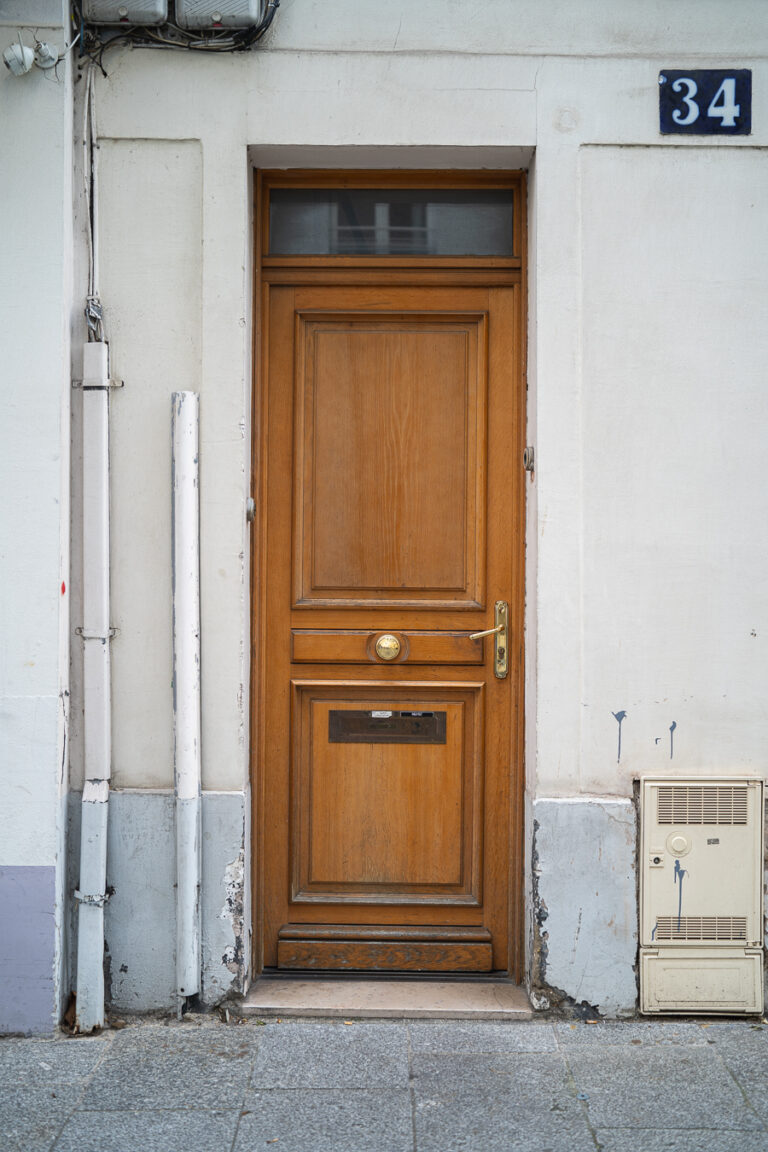 Eine holzgesägte Paneeltür in einer weißen Fassade mit der darüber angebrachten Nummer 34.