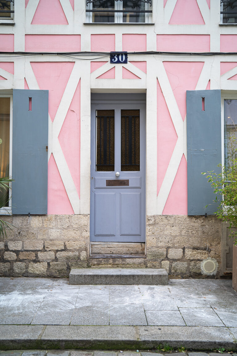 Eine graue Holztür mit der Hausnummer 30 darüber, eingebettet in eine rosa-weiße Fachwerkfassade.
