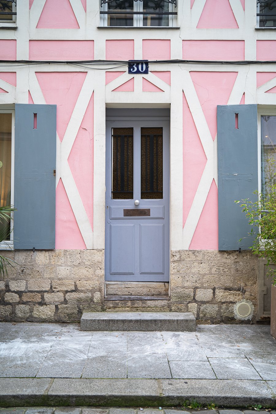 Eine graue Holztür mit der Hausnummer 30 darüber, eingebettet in eine rosa-weiße Fachwerkfassade.