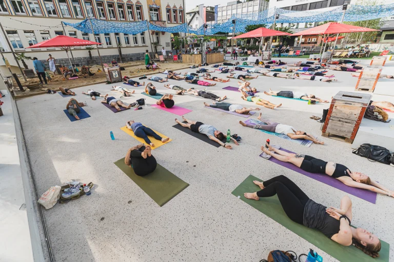 A large group of people lying on yoga mats on a paved public square during an outdoor session.