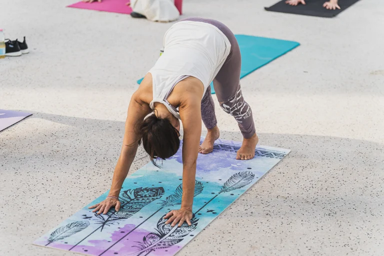 A woman performs a downward-facing dog yoga pose on a patterned mat outdoors.