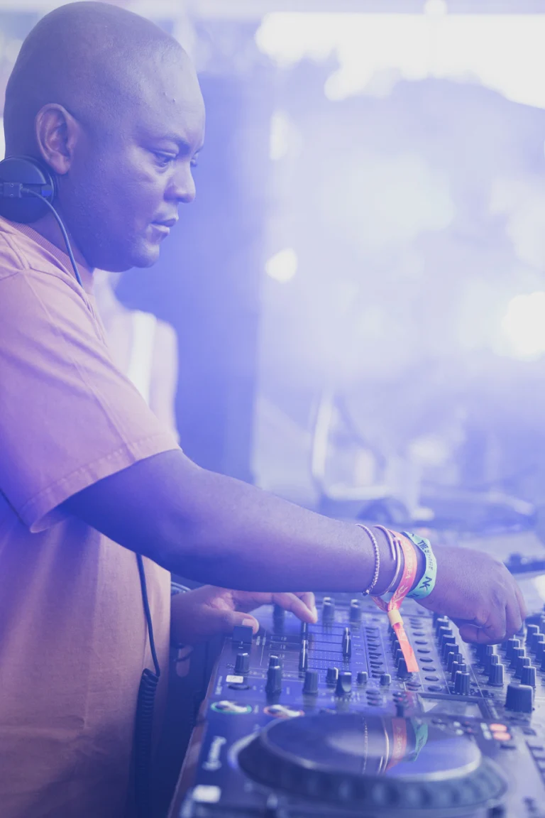 A man wearing headphones operates a mixing console in a purple-tinted, hazy atmosphere.