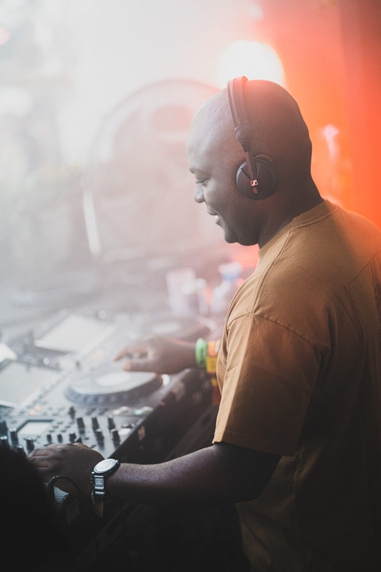 Ein Mann mit Kopfhörern bedient ein Mischpult in dunstigem, warmem Licht.