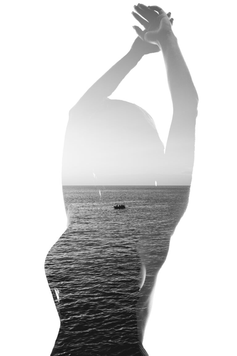 Monochrome double exposure showing the silhouette of a woman raising her arms, overlaid with a seascape and a small boat on the water.