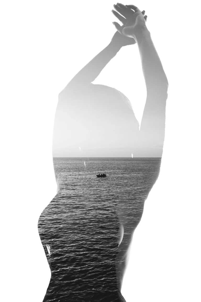 Monochrome double exposure showing the silhouette of a woman raising her arms, overlaid with a seascape and a small boat on the water.