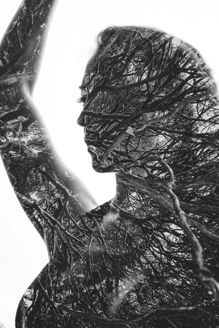 Double exposure portrait of a woman combined with bare tree branches in black and white.
