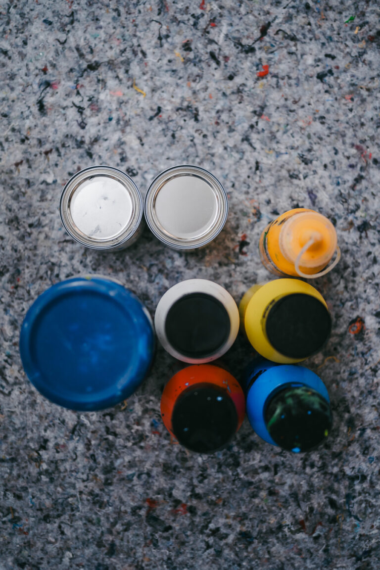 Top-down view of paint cans and squeeze bottles arranged on a speckled grey felt surface.
