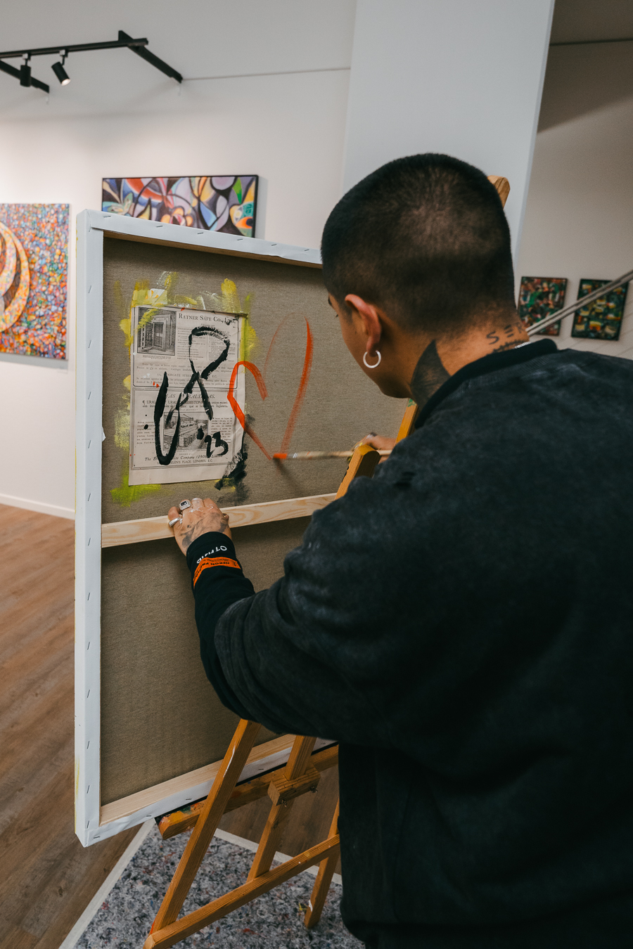 A man paints a red heart on a canvas resting on a wooden easel inside a gallery.