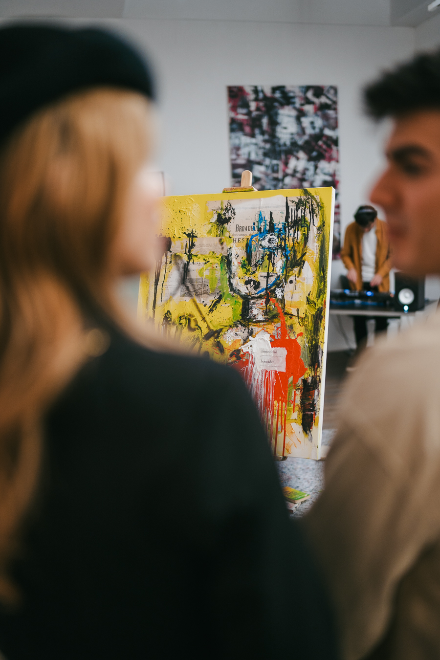 A woman and a man look towards an abstract painting on an easel in a bright room.