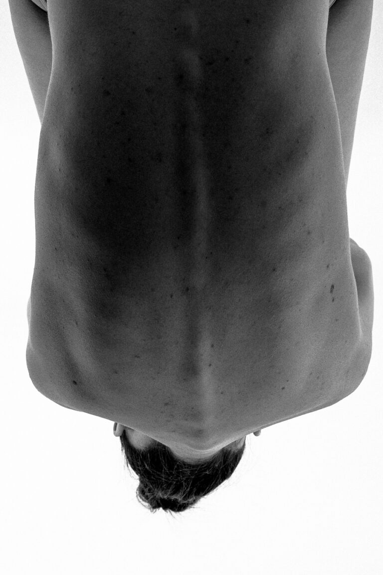 Monochrome close-up of a woman's bare back with dark hair tied in a bun at the bottom.
