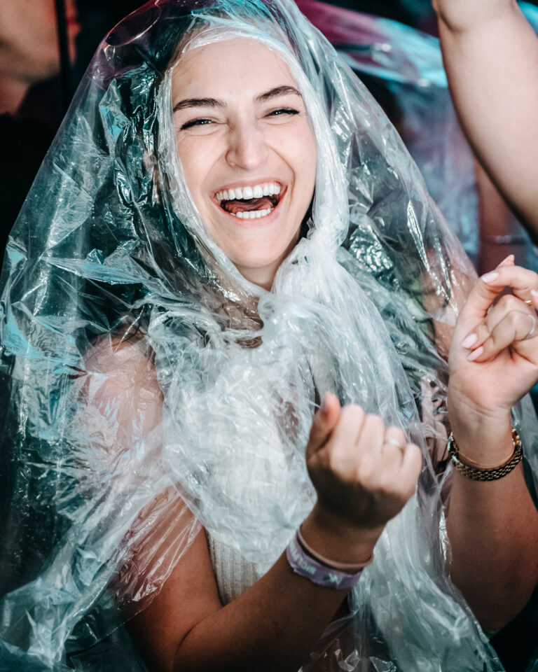 Eine lachende Frau trägt einen durchsichtigen Plastikponcho über Kopf und Schultern.