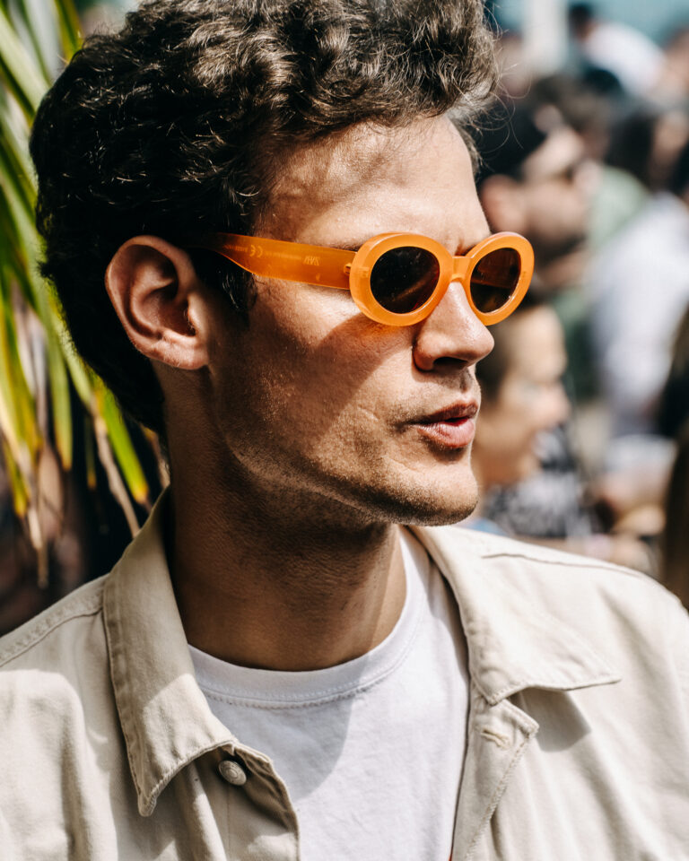 Nahaufnahme im Profil eines Mannes mit runden orangefarbenen Sonnenbrillen und einem weißen T-Shirt im hellen Tageslicht.