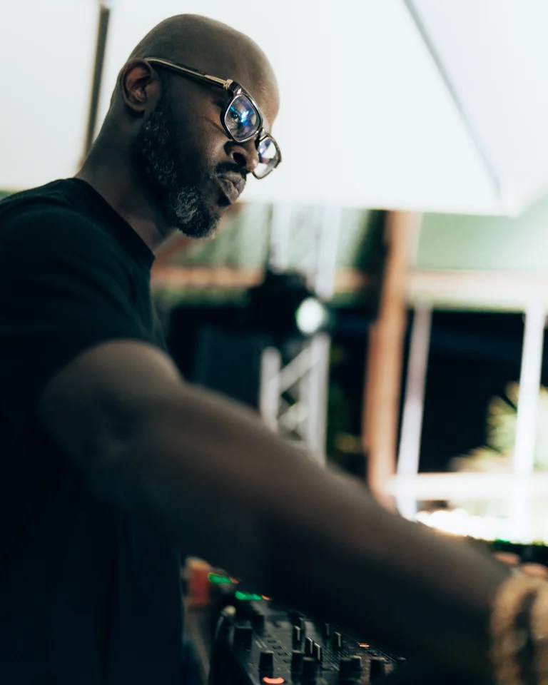 A bald man wearing glasses and a dark shirt leans over a mixing console.