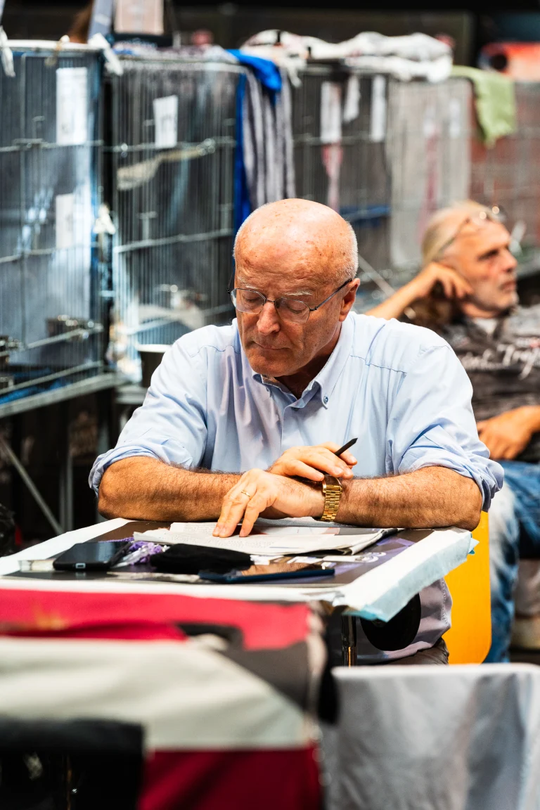 A bald man wearing glasses and a light blue shirt sits at a desk, looking down at documents.