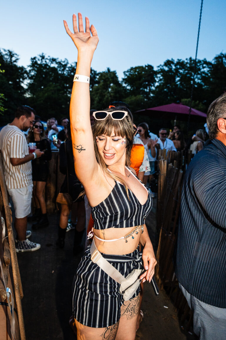 A woman in a striped outfit raises her arm in a crowd outdoors.