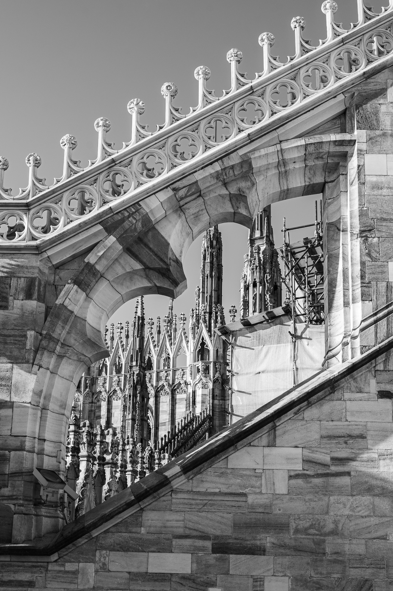 Schwarz-Weiß-Ansicht aus der Froschperspektive mit filigranen gotischen Architekturdetails und den Türmen des Mailänder Doms.