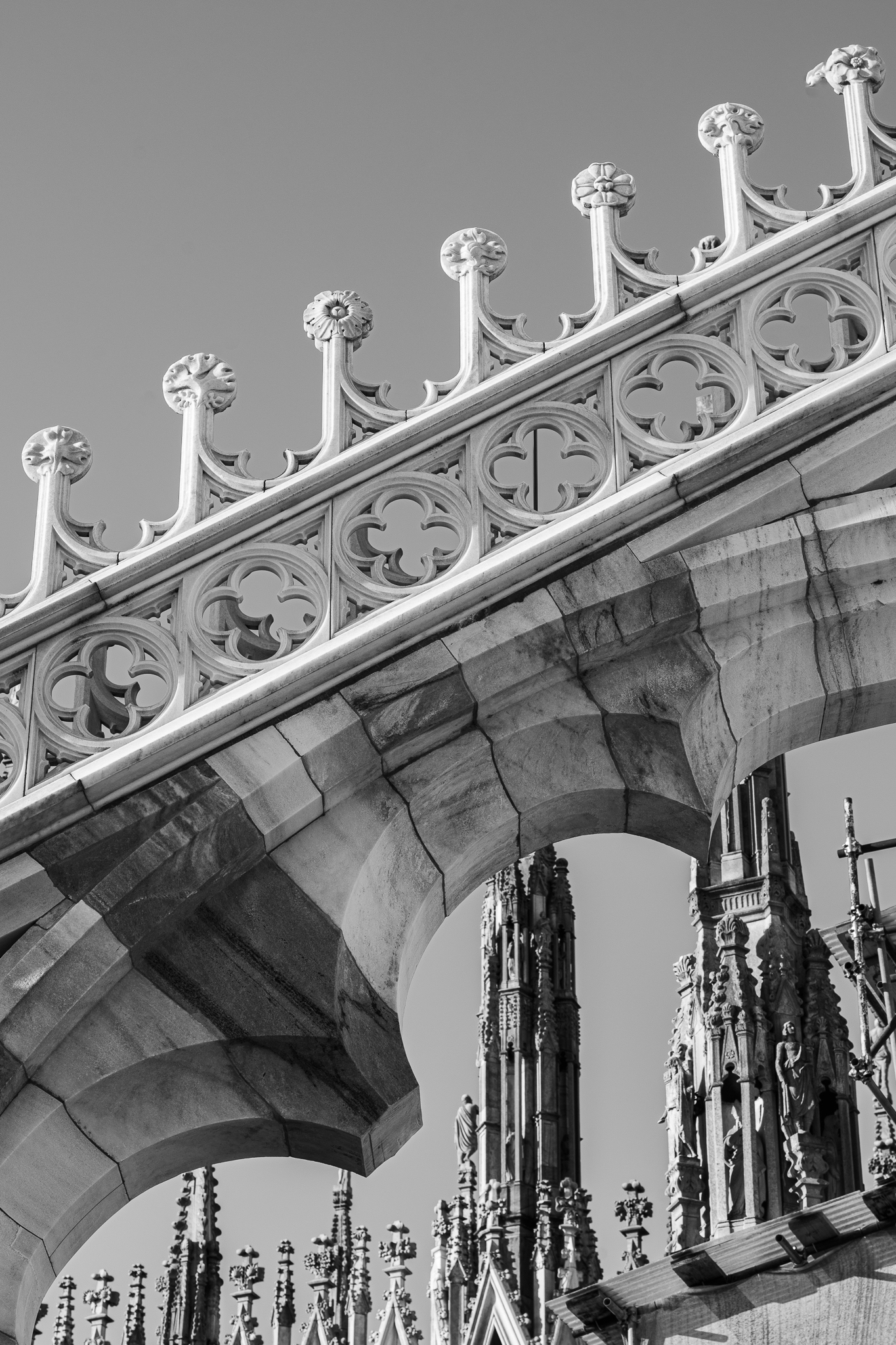 Schwarz-Weiß-Ansicht von unten auf detailreiche gotische Architekturelemente und Spitzbögen des Mailänder Doms vor klarem Himmel.