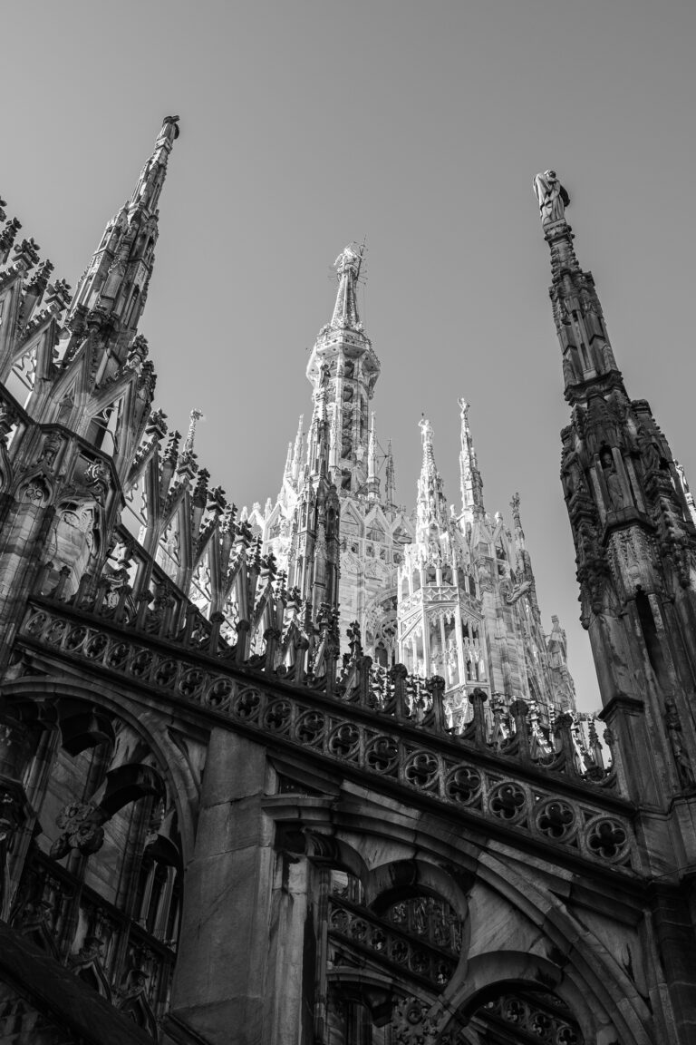 Schwarz-Weiß-Ansicht aus einer Froschperspektive auf filigrane gotische Türme und verzierte Steinarchitektur des Mailänder Doms.