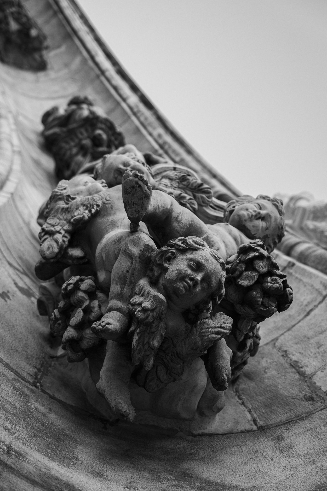 Eine Schwarz-Weiß-Fotografie aus niedriger Perspektive zeigt detailreiche Steinschnitzereien von Putten und Blattwerk, die architektonische Elemente des Mailänder Doms schmücken.