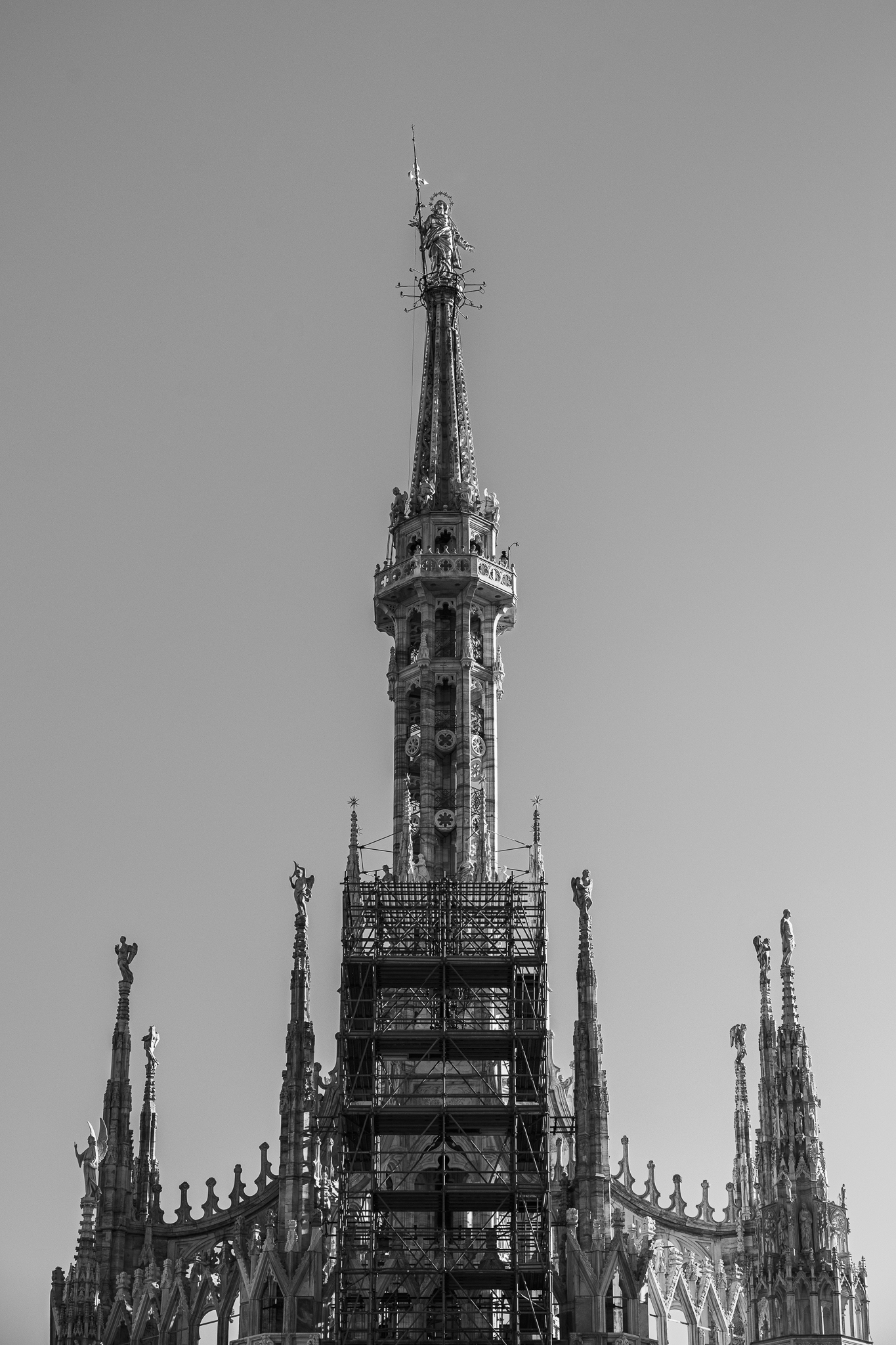 Schwarz-Weiß-Ansicht der Turmspitze des Mailänder Doms aus der Froschperspektive, umgeben von Gerüsten.