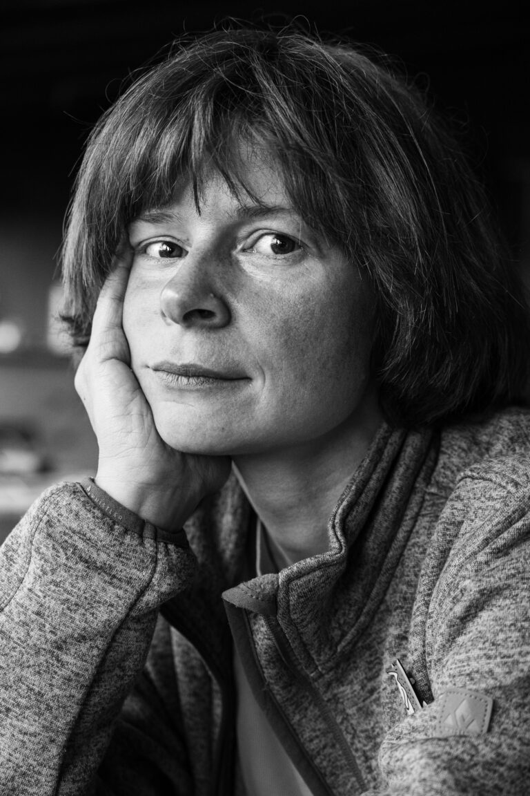 Close-up monochrome portrait of a woman resting her cheek on her hand, looking directly at the camera.