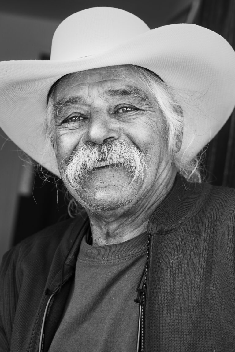 Fekete-fehér portré egy idős férfiról, aki fehér bajuszt és cowboykalapot visel.