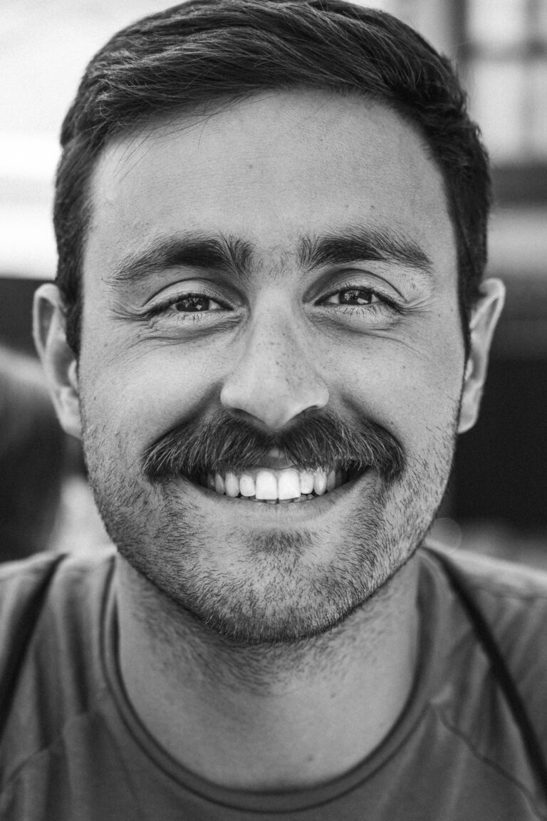 Close-up monochrome portrait of a smiling man with a thick mustache.