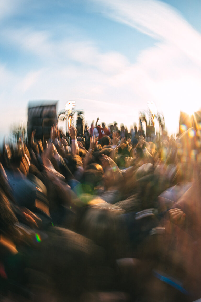 A fisheye, motion-blurred view of a crowd with raised hands under bright daylight.
