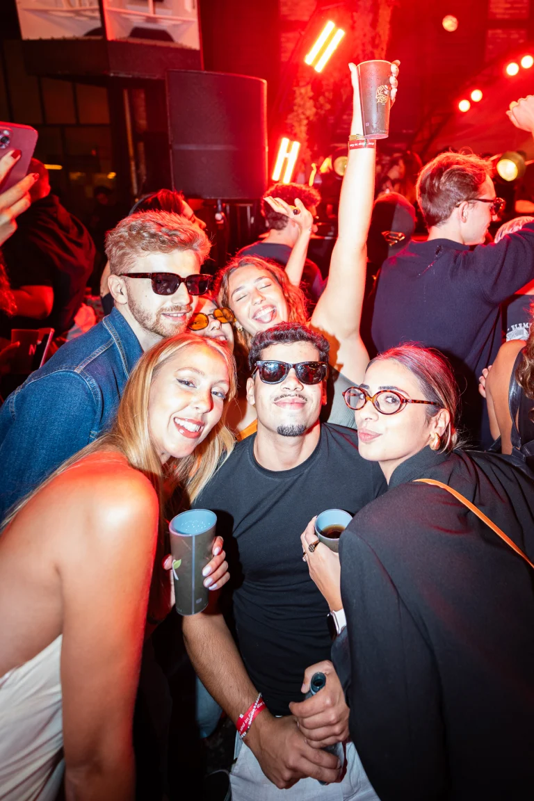 A close-up view of a group of young men and women smiling and holding cups in a brightly lit indoor venue.