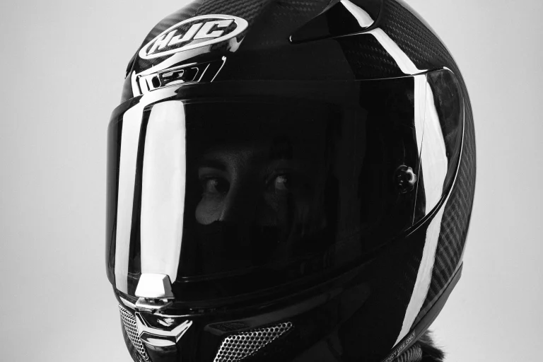 A black and white close-up of a woman wearing a black HJC motorcycle helmet with her eyes visible through the dark visor.