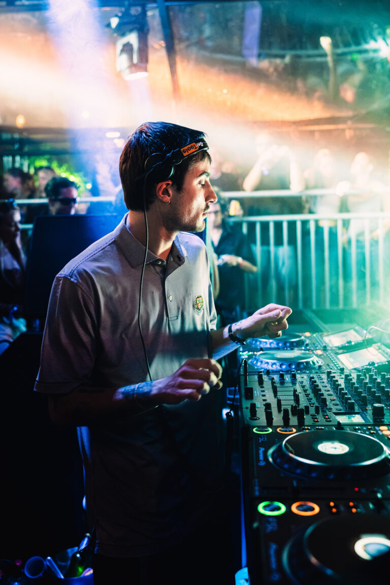 A man wearing headphones operates a mixing console in a brightly lit club setting.