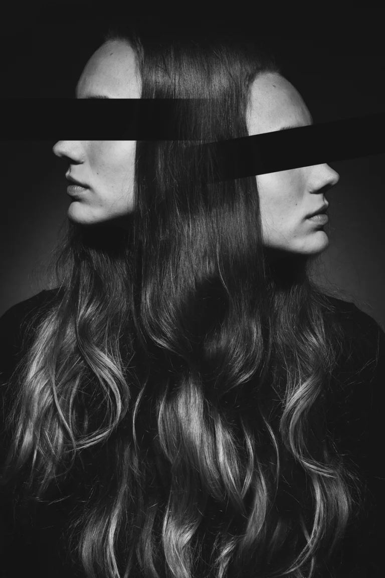 Monochrome studio portrait of a woman shown in profile, merged with a second flipped profile, with horizontal black bands covering their eyes.