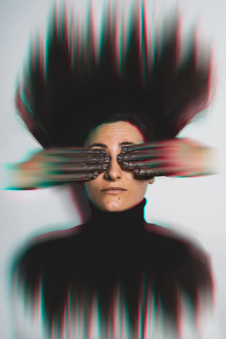 A woman covering her eyes with motion-blurred hands against a white background, featuring a strong glitch and chromatic aberration effect on her hair and figure.