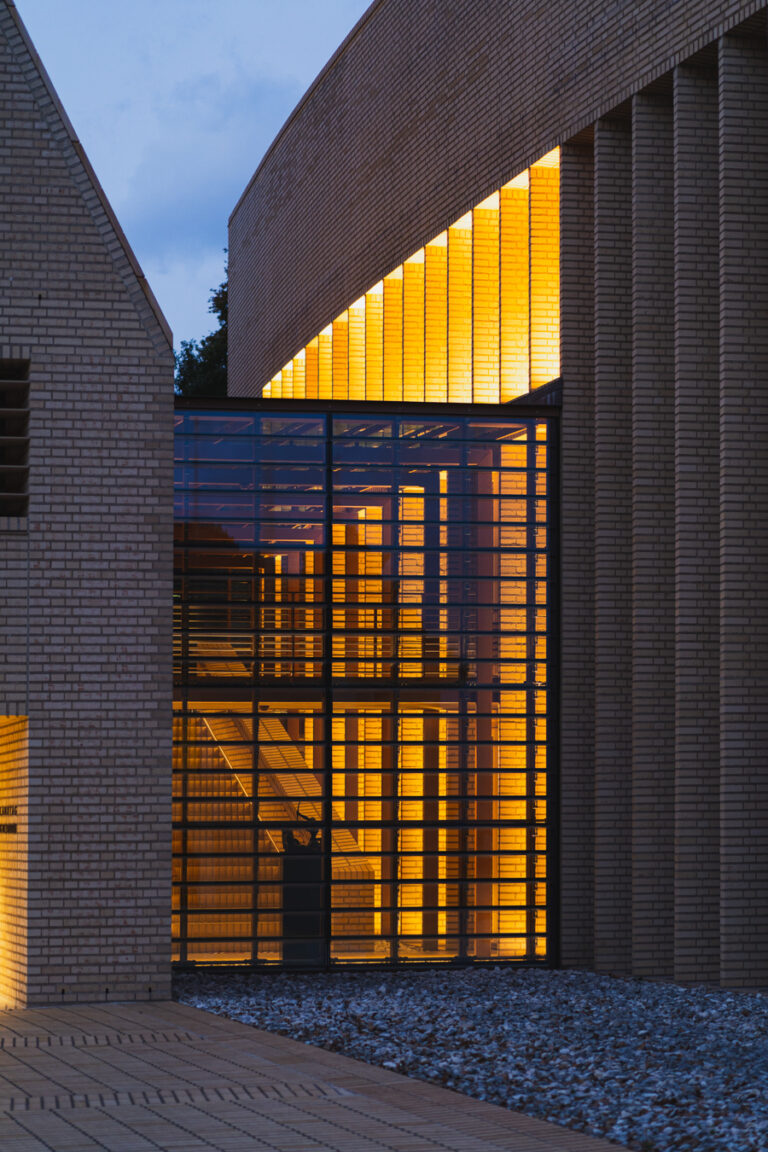 View of the Vaduz Parliament building at dusk, featuring a large glass connector between brick structures with warm interior lighting.