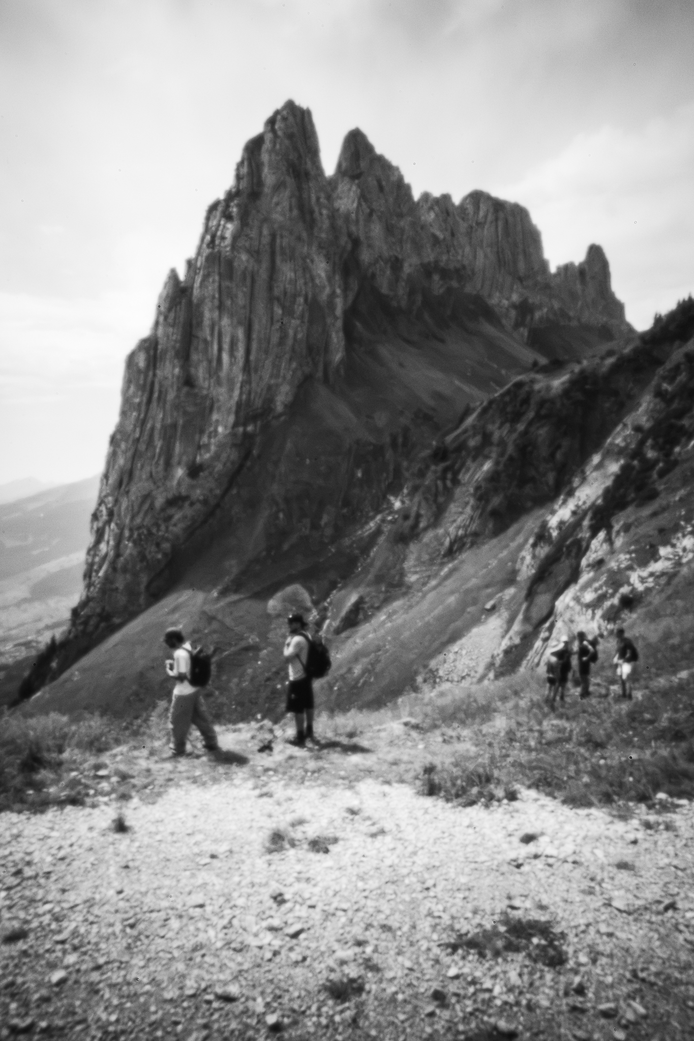 Monochrome, weich gezeichnete Weitwinkelaufnahme von Wanderern auf einem Bergpfad unter den scharfen Gipfeln der Saxer Lücke.