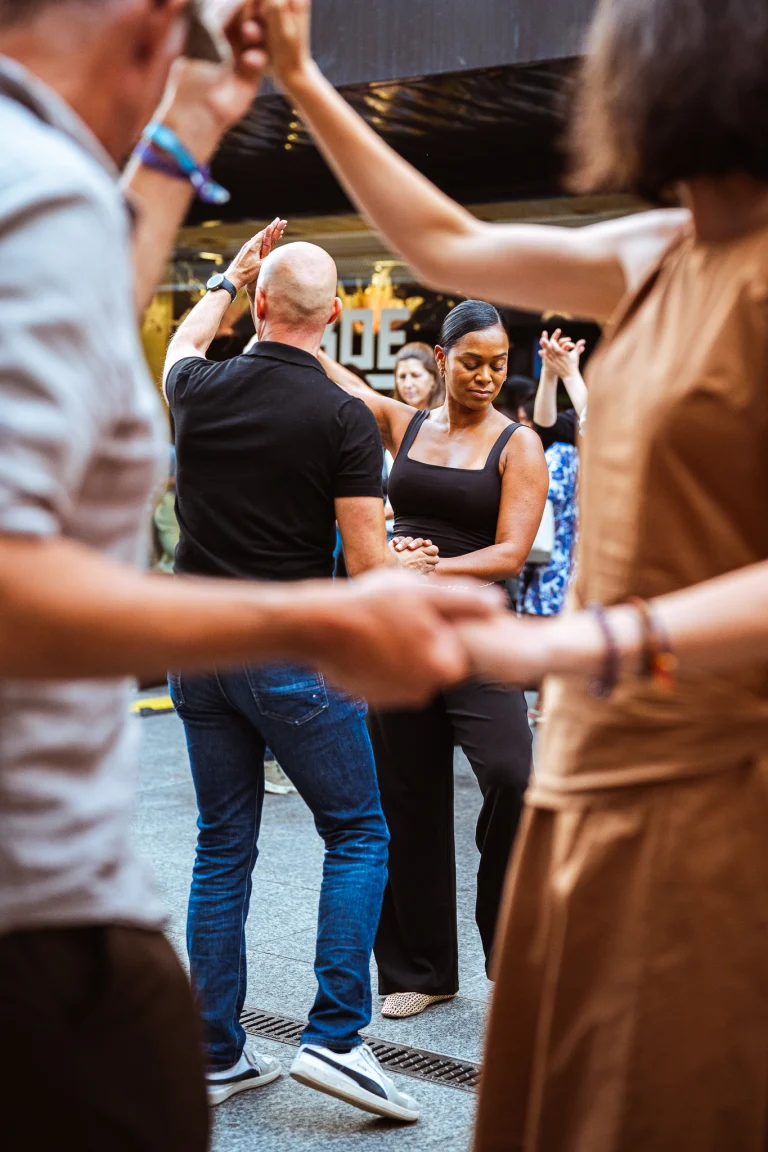 A man and a woman dance together outdoors, framed by other dancers in the foreground.