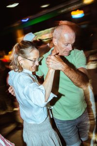 A woman and a man dancing together indoors under motion-blurred lights, holding hands in a close embrace.