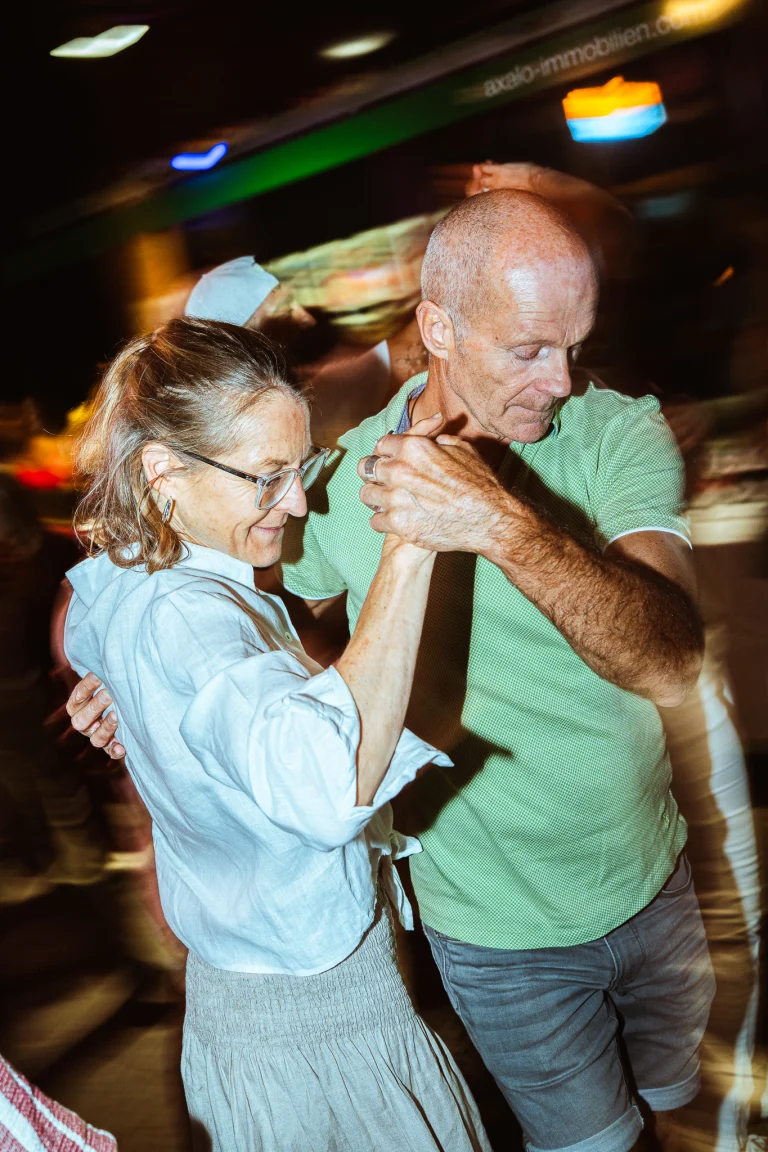 A woman and a man dancing together indoors under motion-blurred lights, holding hands in a close embrace.
